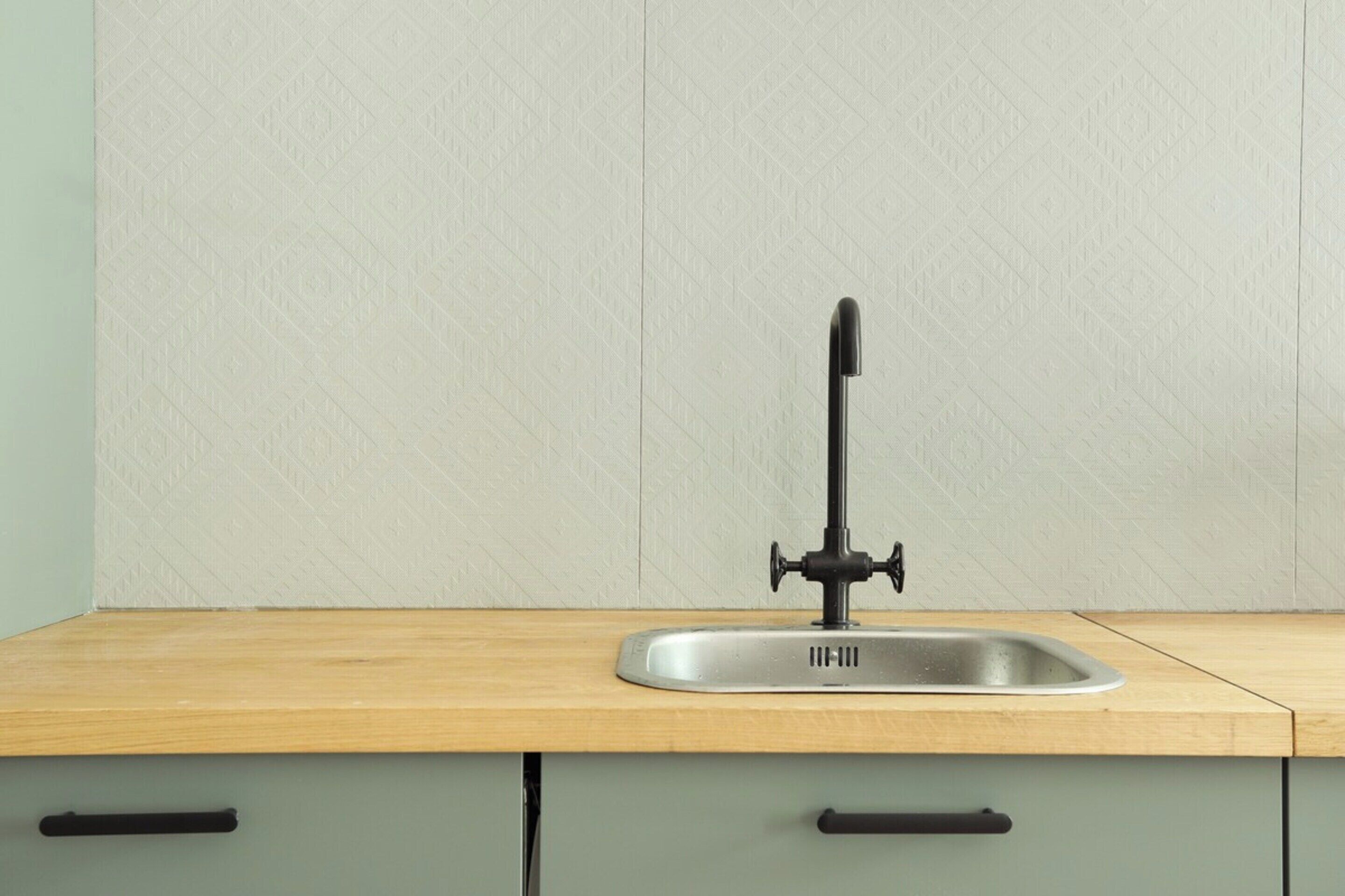 A kitchen with a single stainless steel sink, a wooden countertop, and light green cabinets.