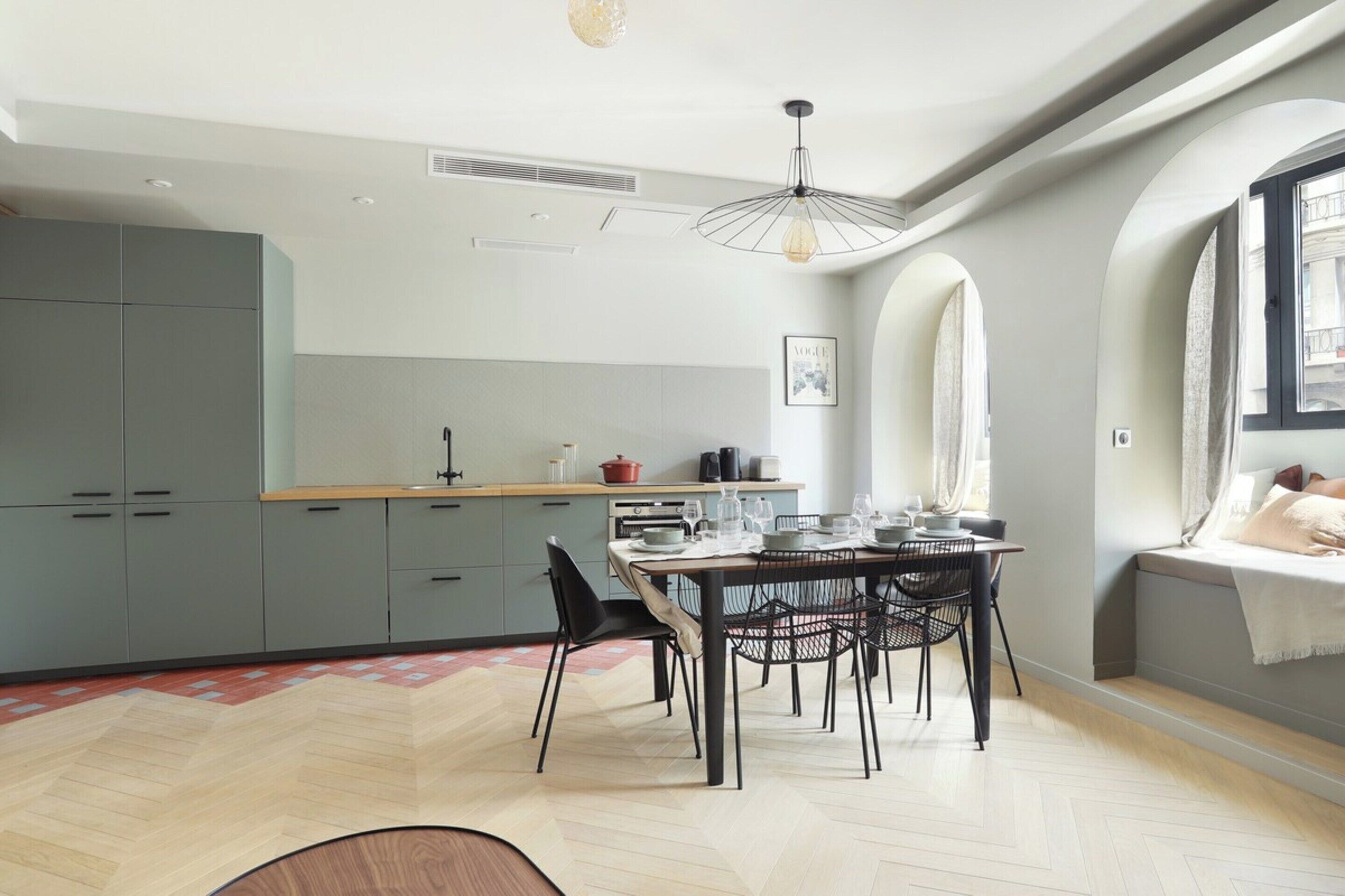 Une cuisine moderne avec des meubles gris, un plan de travail en bois et un coin repas avec une table dressée pour quatre personnes.