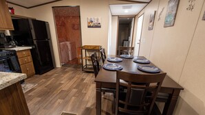 A compact kitchen with a dining area, featuring a wooden table set for four, a refrigerator, and a coffee machine. - Your Peaceful Georgetown Escape (Georgetown)