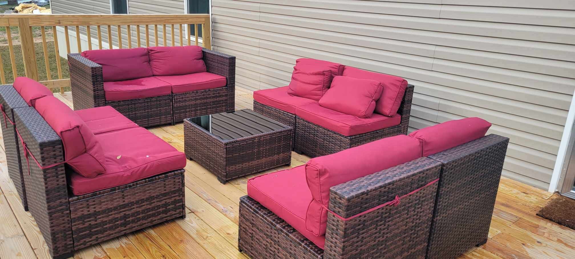 A patio with wicker furniture and red cushions.