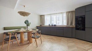 A modern kitchen with a dining area, featuring a herringbone wood floor, a green cushioned bench, and a pendant light. - Spacious AC Flat Luxembourg St Germain des Pres (Paris)