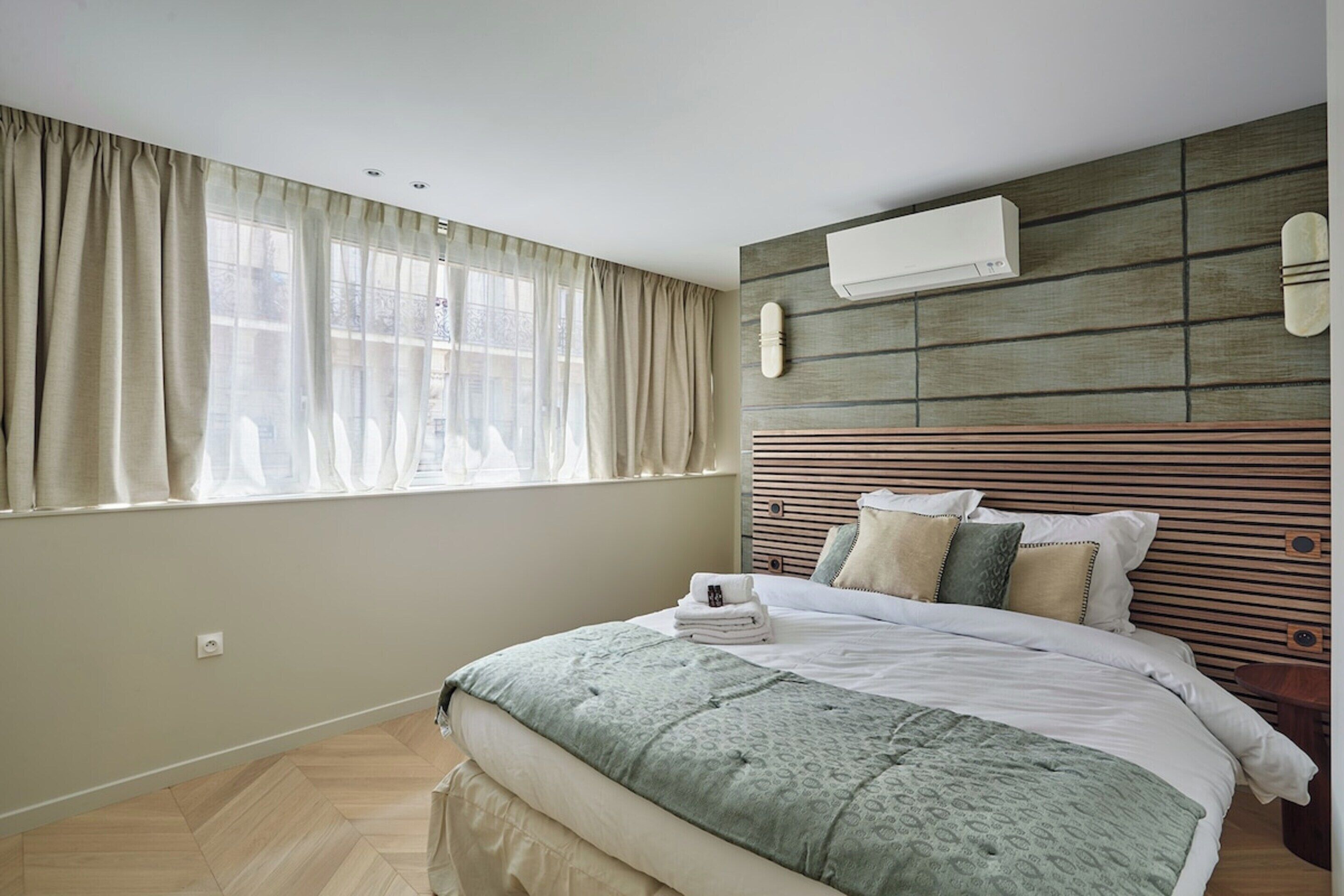 Ein Schlafzimmer mit einem Bett, einem Fenster mit Vorhängen, einer Klimaanlage und einem hölzernen Kopfteil.