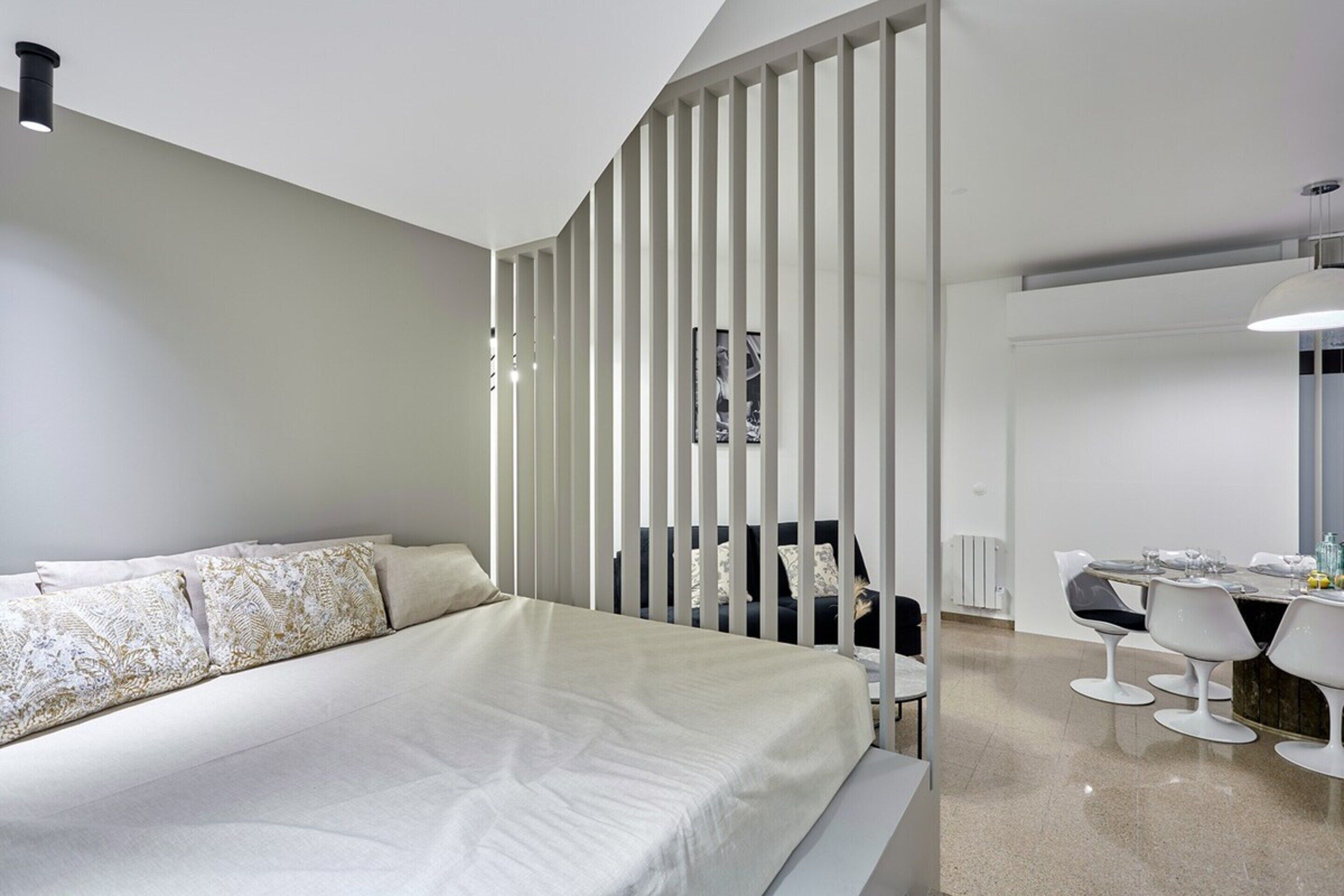 A modern bedroom with a large bed, a desk with chairs, and a white partition.