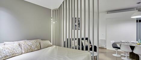 A modern bedroom with a large bed, a desk with chairs, and a white partition.