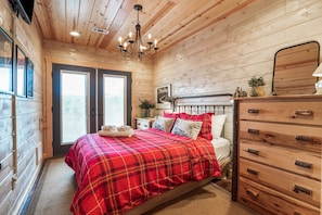 A bedroom with a plaid bedspread, wooden walls, a dresser, and a chandelier.