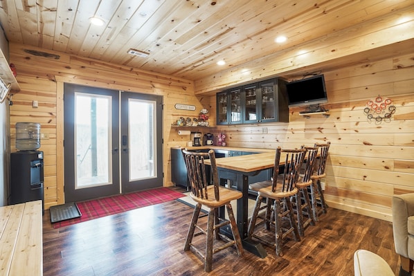 A wooden cabin interior with a dining area, kitchen, and a coffee bar.