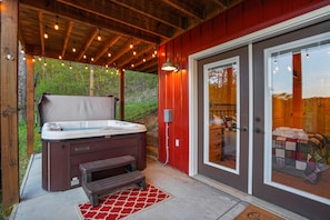 Un jacuzzi con un banco de madera, una pared exterior roja y una puerta que da a un patio cubierto.