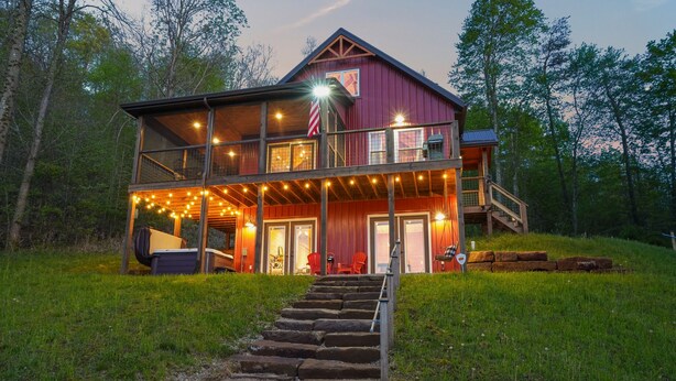 A two-story wooden cabin with a porch, outdoor seating, and a staircase leading to the entrance.