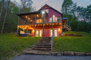 Een houten chalet met twee verdiepingen, een veranda, zitplaatsen buiten en een trap naar de ingang.