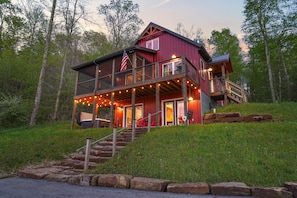 A two-story cabin with a balcony, wooden deck, and string lights.