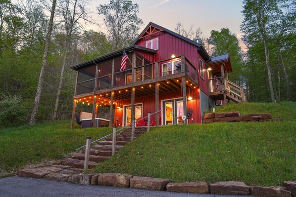 A two-story cabin with a balcony, wooden deck, and string lights.