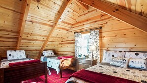 A cozy cabin bedroom with two beds, a wooden ceiling, and a window with patterned curtains.