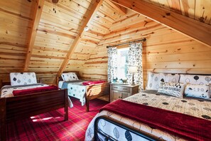 A cozy cabin bedroom with two beds, a wooden ceiling, and a window with patterned curtains.