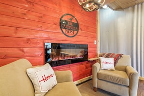 Un cuarto acogedor con una pared de madera roja, una chimenea, dos sillones beige y una almohada con la palabra 'Home' en uno de los sillones.