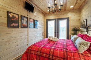 Una habitación con paneles de madera, una cama, carteles enmarcados, un televisor y una araña.