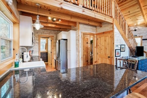 A spacious kitchen with a granite countertop, wooden ceiling beams, and a built-in refrigerator.