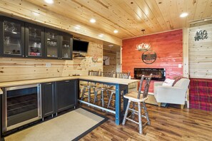 A wooden interior with a kitchen area, dining table, chairs, and a fireplace.