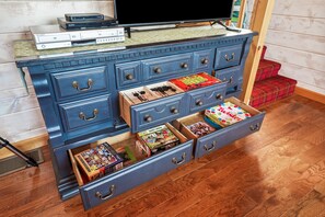 Un comò blu con diversi cassetti, una televisione sopra e vari giochi da tavolo e giocattoli nei cassetti.