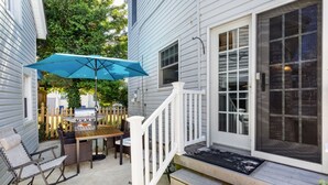 A patio with a grill, outdoor seating, and a blue umbrella.