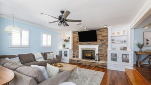 A living room with a stone fireplace, a ceiling fan, and a TV mounted above it.