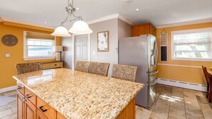 A kitchen with a granite island, stainless steel refrigerator, and pendant lighting.