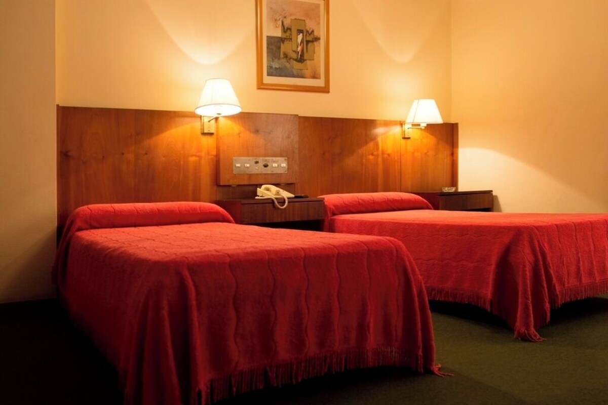 A hotel room with two beds, wooden headboard, bedside lamps, a telephone, and a painting on the wall.