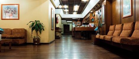 Un vestíbulo de hotel con piso de madera, un mostrador de recepción y zonas de estar.