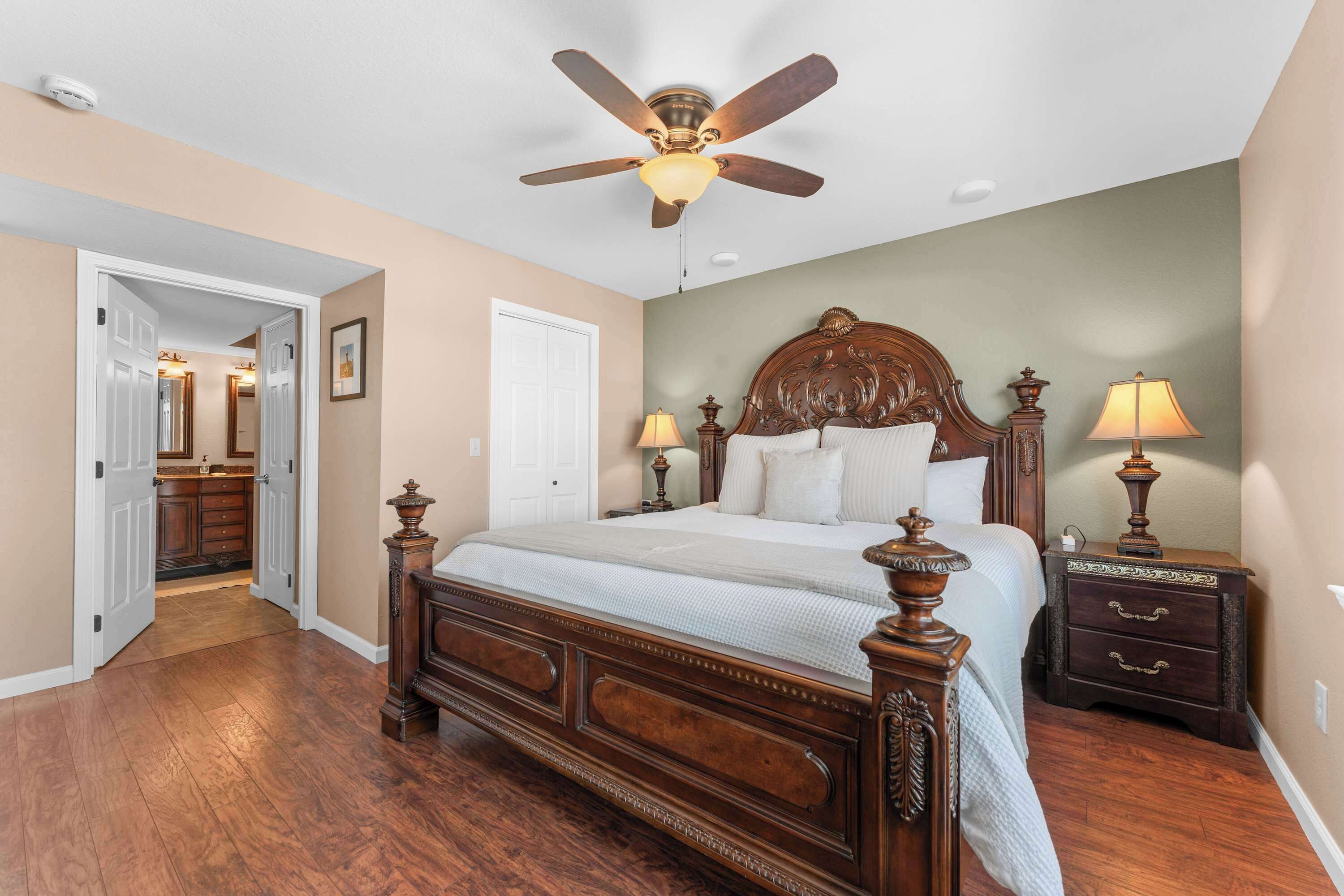 Quarto com cama de madeira, ventilador de teto, duas luminárias de cabeceira e mesa de cabeceira com gavetas.