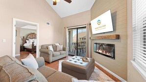 A modern living room with a fireplace, a ceiling fan, and a large TV screen displaying a welcome message. - Branson Blessing Condo for 8! (Branson)