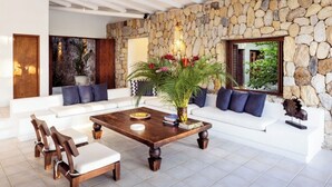 A modern living room with a stone wall, white sofas, wooden coffee table, and a large plant. - Yeguas V43 by Wynwood House (Anapoima)