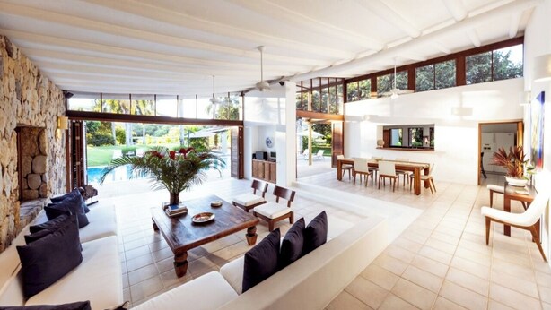 A spacious living area with a stone wall, a wooden dining table, and a pool visible through large windows. - Yeguas V43 by Wynwood House (Anapoima)