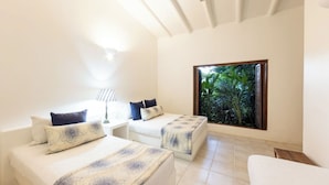 A room with two beds, a small table, and a large window with a view of greenery. - Yeguas V43 by Wynwood House (Anapoima)