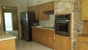 Una cocina con gabinetes de madera, un refrigerador de acero inoxidable, un horno empotrado y una pared de acento de ladrillo.
