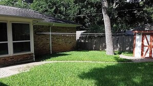 Un patio trasero con una casa de ladrillo, cerca de madera y un árbol.