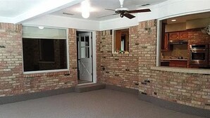 Una habitación con paredes de ladrillo, un ventanal grande, una puerta y un ventilador de techo.