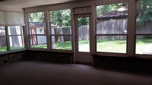 Una habitación con ventanas amplias, una pared de piedra y una puerta que da al exterior.