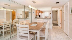 Een eethoek met een houten tafel en witte stoelen, een keuken op de achtergrond, en een glazen scheidingswand.