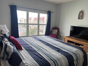 A hotel room with a large bed, a TV on a wooden stand, a chair, and a window with curtains.