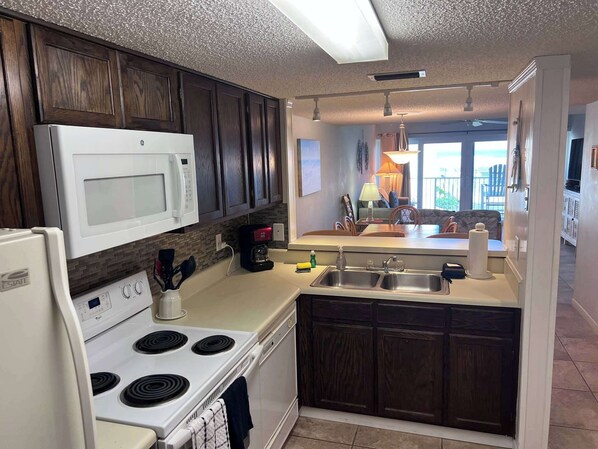 A kitchen with dark wood cabinets, a white stove, a microwave, and a sink.