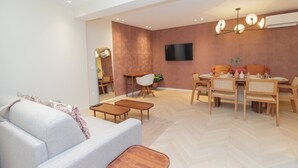 A modern living room with a sofa, coffee table, dining table with chairs, and a TV mounted on the wall. - Elegant Apartment St Germain des Pres Luxembourg Park (Paris)
