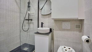 Une salle de bain moderne dotée d’une douche à parois de verre, d’un lavabo blanc avec un plan de toilette noir et de toilettes avec un porte-rouleau de papier toilette.