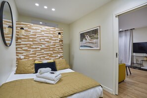 Ett hotellrum med en säng, en spegel som hänger på väggen, en tavla och en tv.