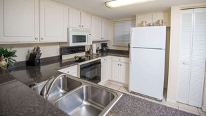 A kitchen with white cabinets, a microwave, a refrigerator, and a sink.