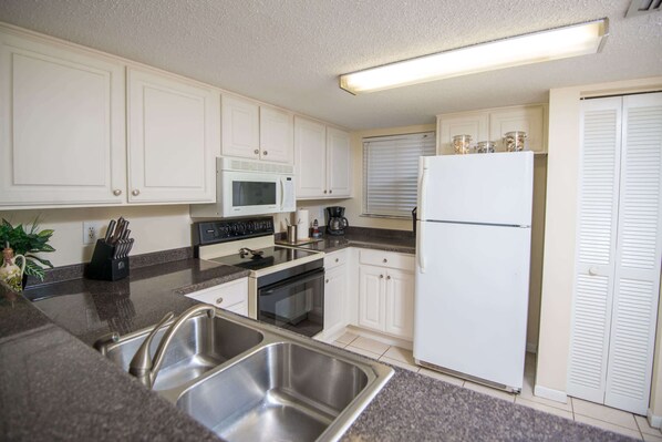 A kitchen with white cabinets, a microwave, a refrigerator, and a sink. - Pier Point South Ocean View Condo D-47 (St. Augustine)