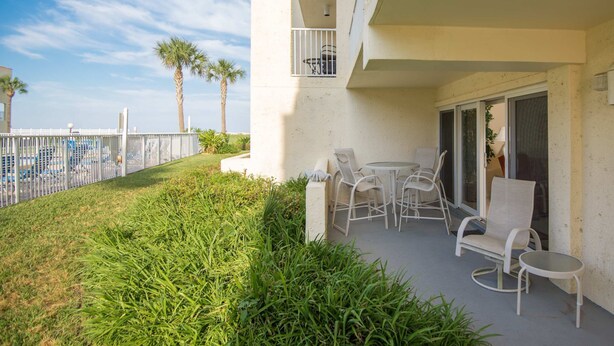 A balcony with outdoor seating, a small window, and a view of the pool and palm trees.