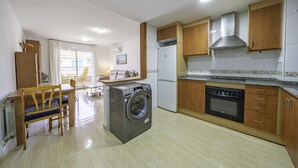 A compact kitchen with a washing machine, a refrigerator, and wooden cabinets. - HomeHolidaysRentals Belisa - Costa Barcelona (Pineda de Mar)