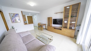 A modern living room with a sofa, TV, wooden cabinet, and a glass coffee table. - HomeHolidaysRentals Belisa - Costa Barcelona (Pineda de Mar)