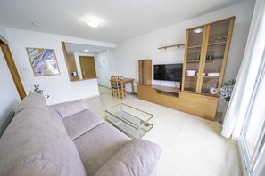 A modern living room with a sofa, TV, wooden cabinet, and a glass coffee table.