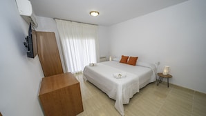 A hotel room with a bed, a wooden desk, a small table with a lamp, and a window with curtains. - HomeHolidaysRentals Belisa - Costa Barcelona (Pineda de Mar)