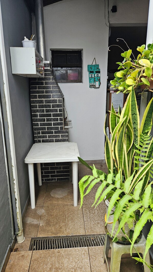A small, enclosed outdoor area with a white bench, a brick wall, a window, and a potted plant.